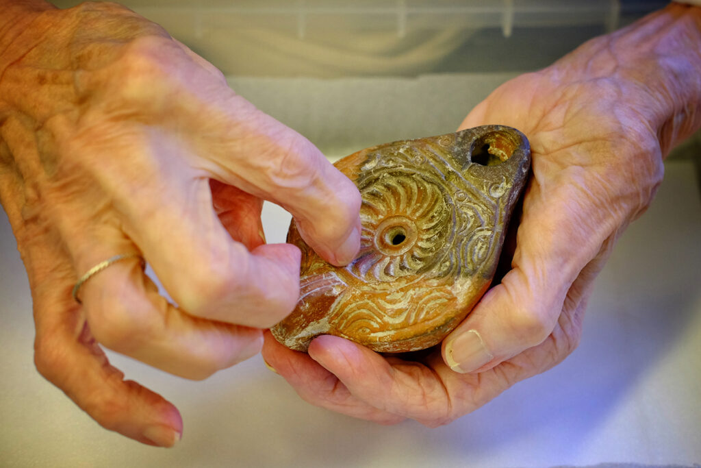A close up of two hands holding part of a Roman oil lamp.
